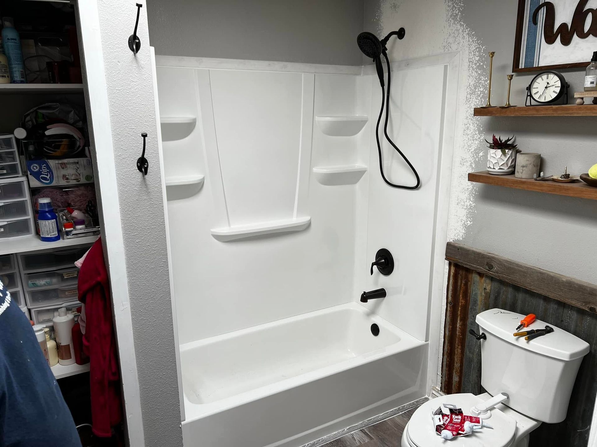 White walk-in shower with built-in shelves and grab bar beside a toilet in a small bathroom.