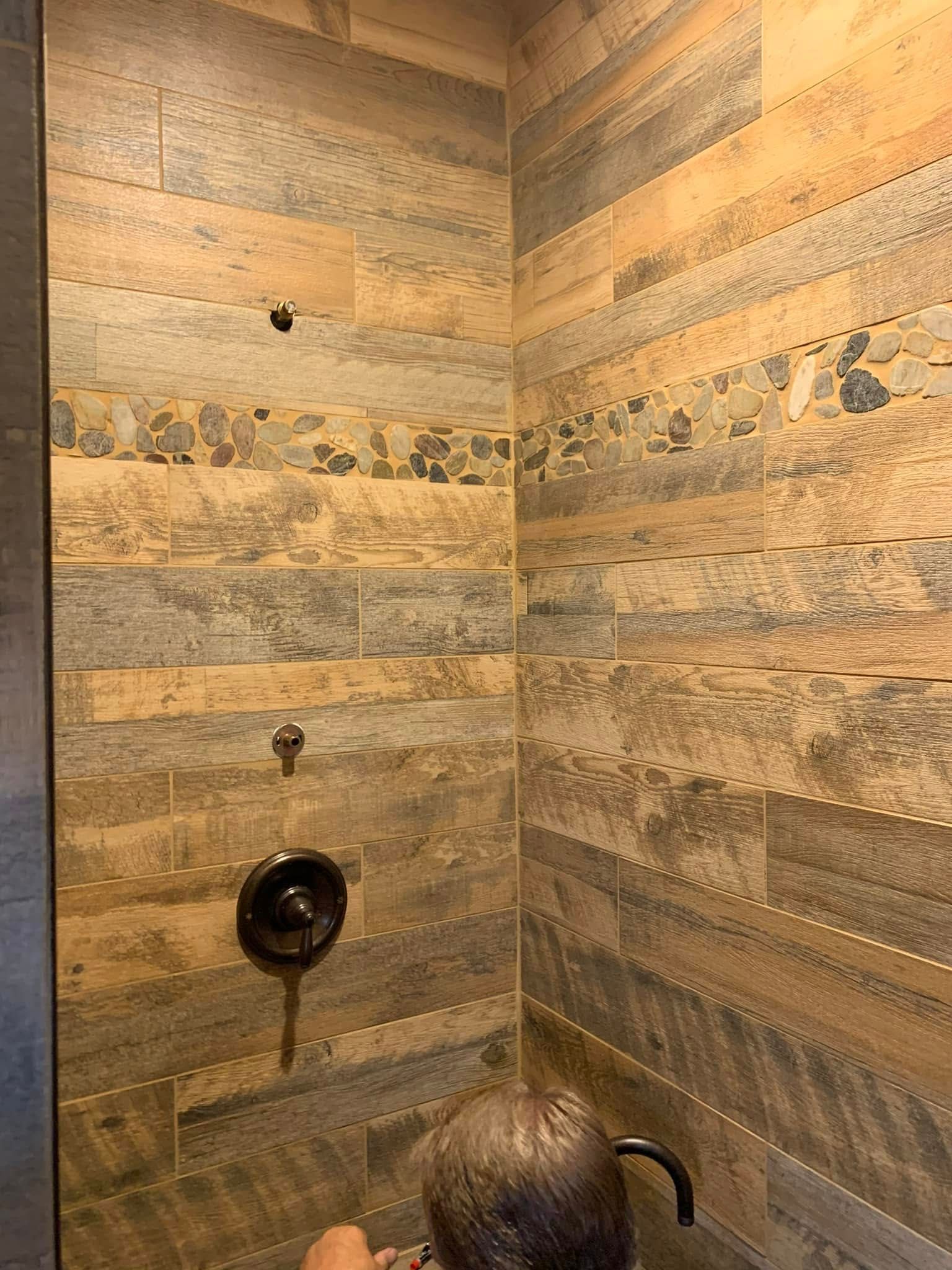 Stone-tiled shower with a wall-mounted showerhead, faucet, and handheld sprayer.