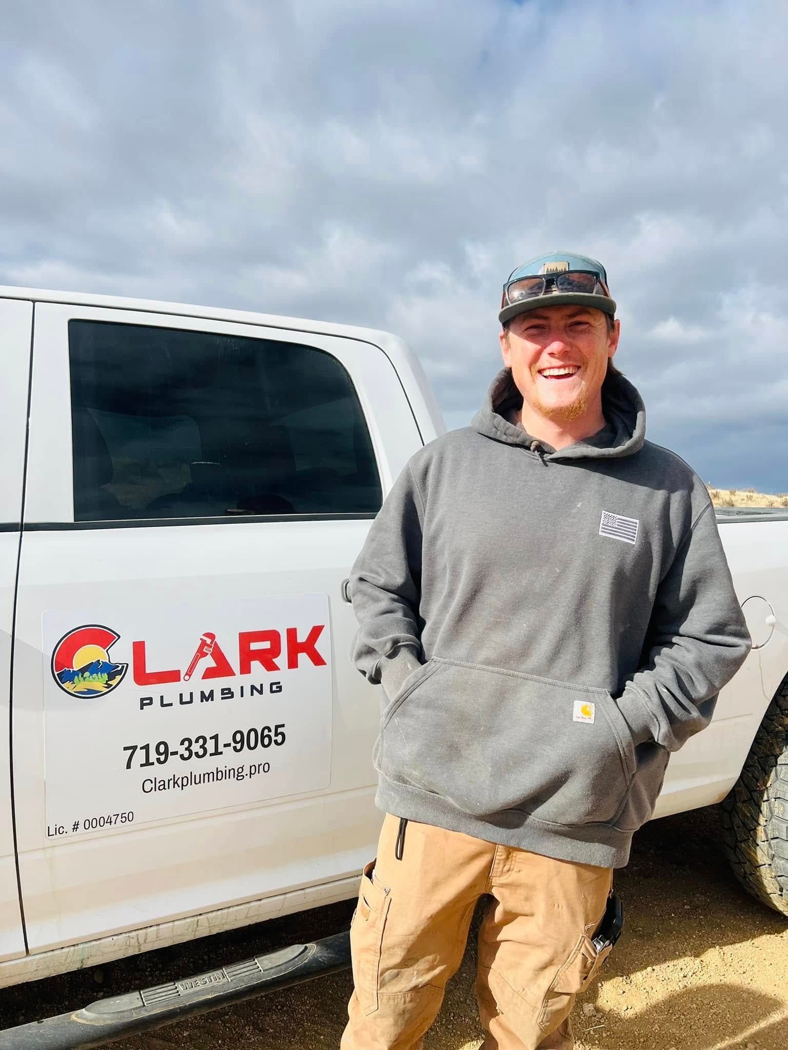 Worker smiling beside white LARK service van, wearing gray hoodie and tan pants.
