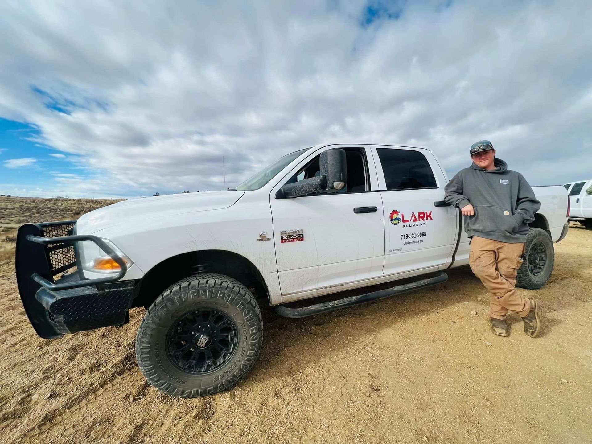 White pickup truck on a dirt road with a man standing beside it under a cloudy sky.