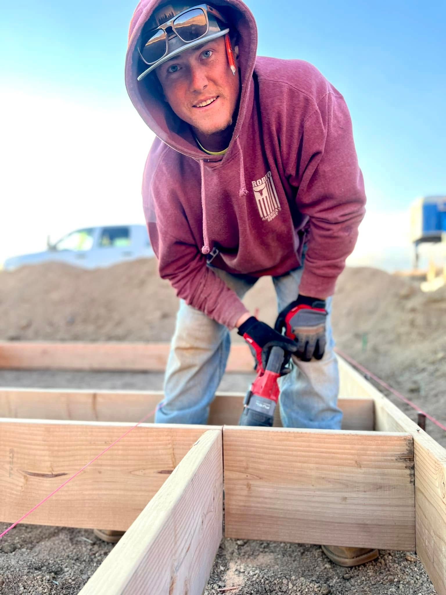 Person in maroon hoodie using a drill on a wooden frame at a construction site