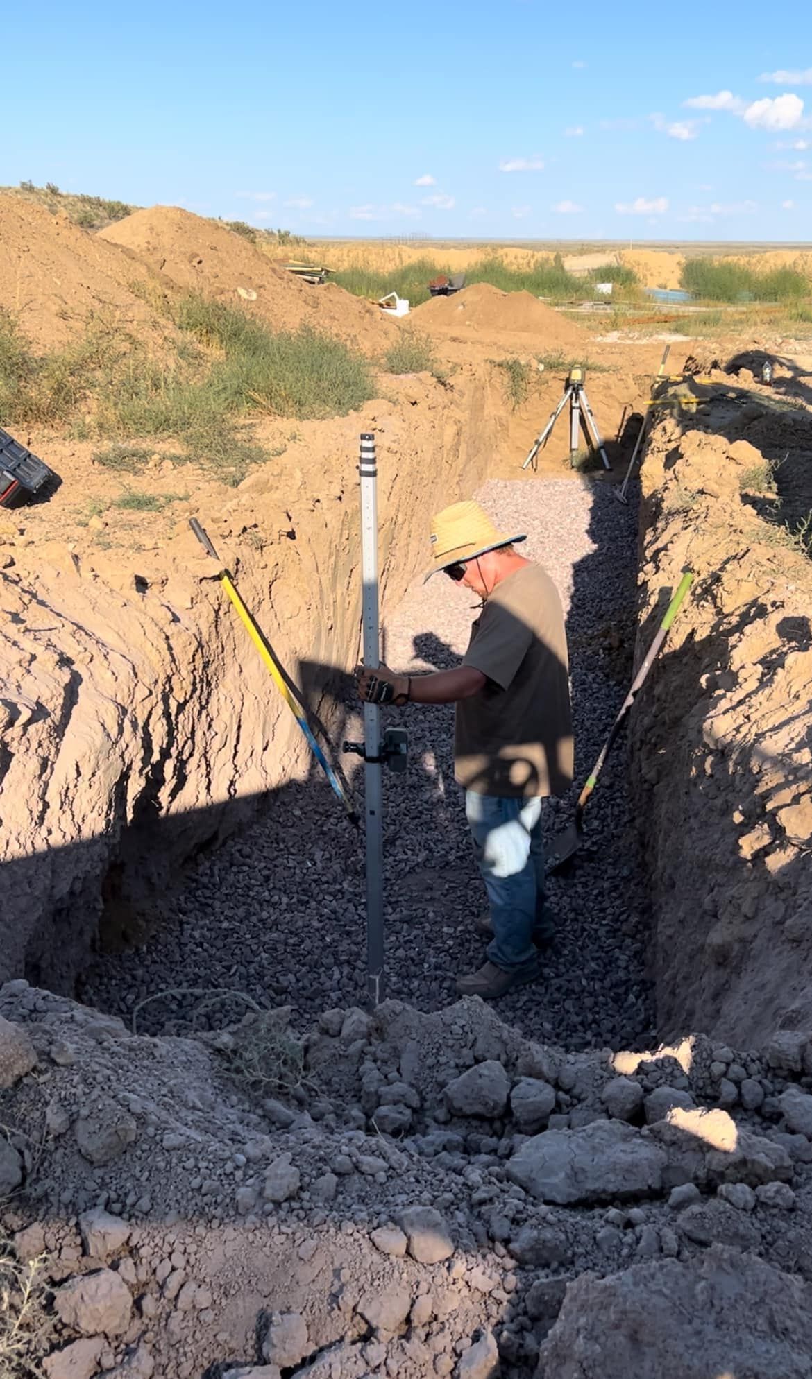 Worker installing a pipe in a trench at a dusty construction site