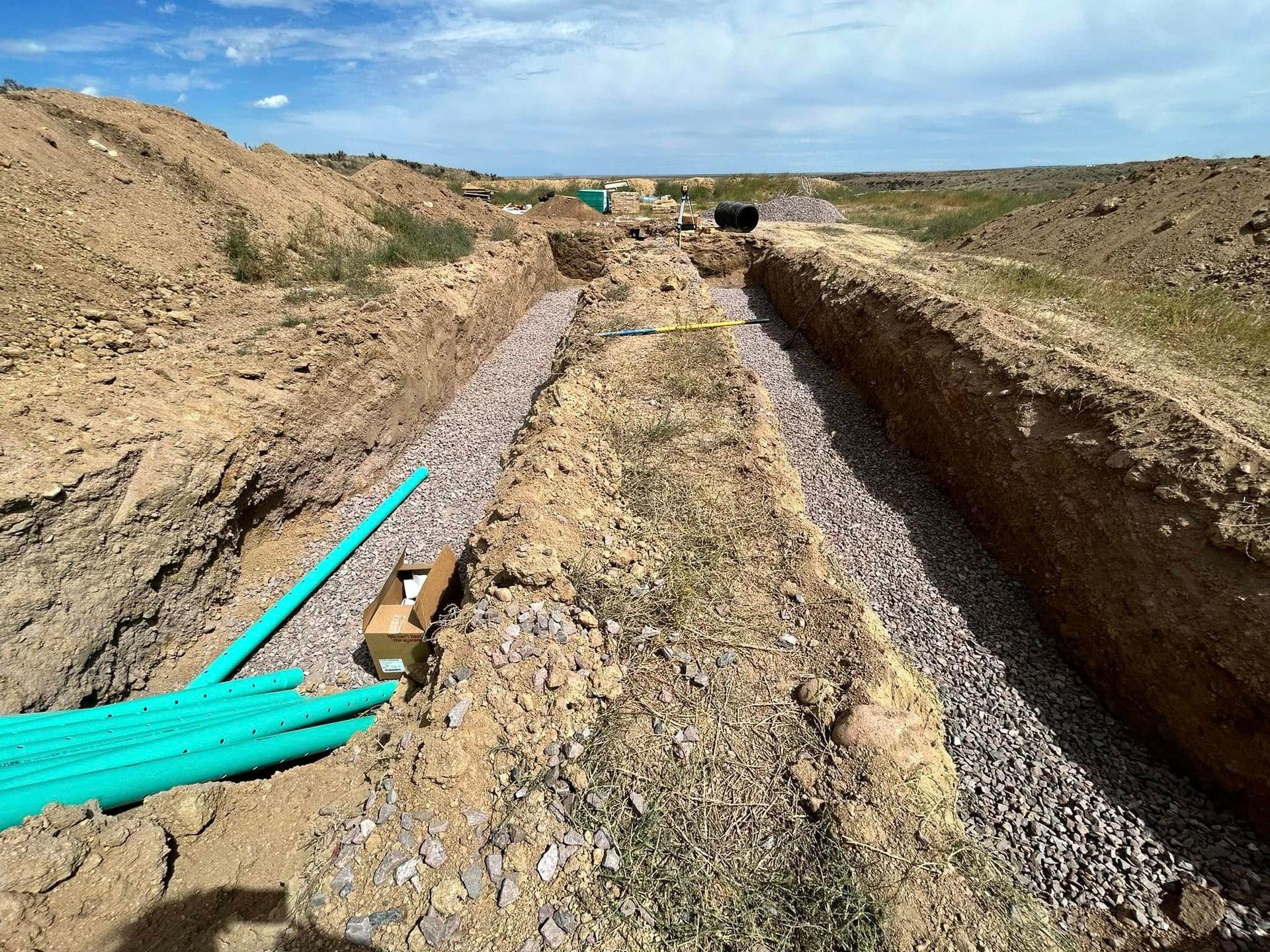 Trenched dirt path with blue pipes laid along the left side in a dry construction site