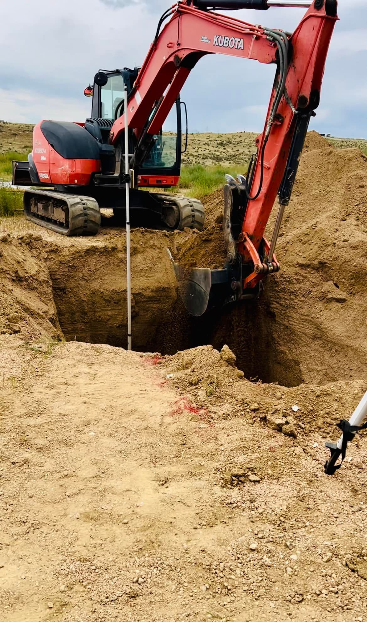 Orange excavator digging a deep hole in sandy ground at a construction site