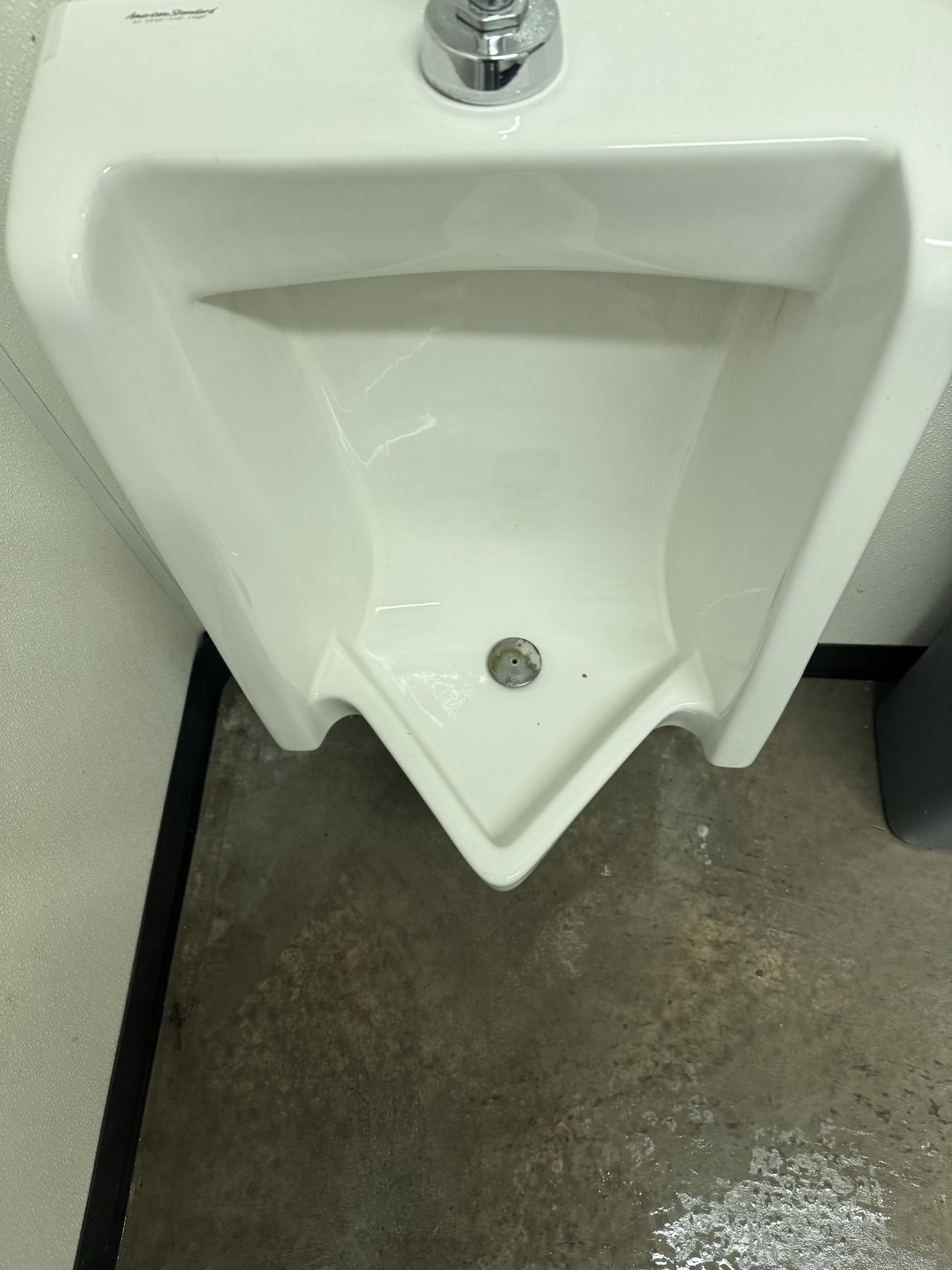 White wall-mounted urinal with silver flush valve in a restroom stall