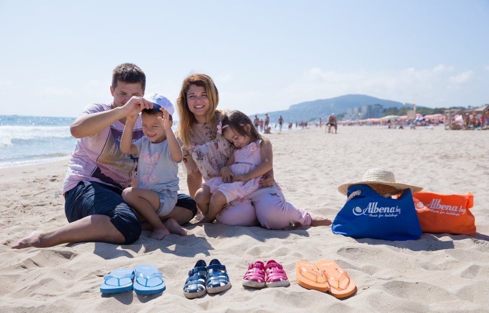 A family is sitting on the beach taking a picture of their shoes.