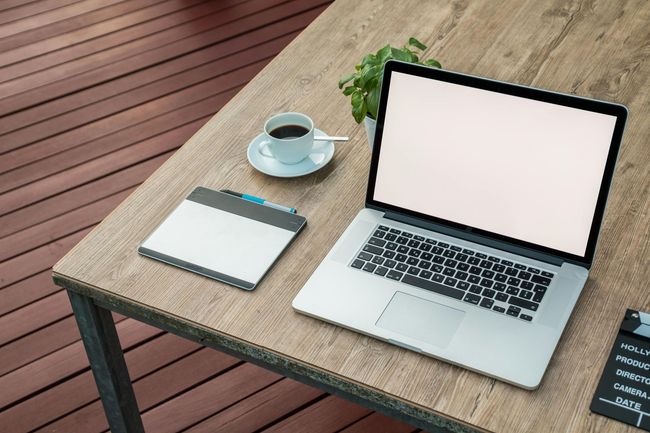 A laptop computer is sitting on a wooden table next to a cup of coffee.