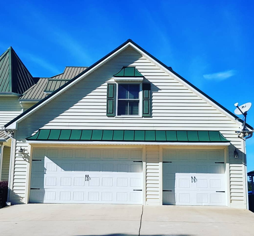 Two-story white house with green trim and two white garage doors under a bright blue sky