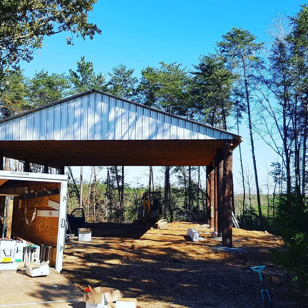 Open-sided metal shed in a wooded clearing under a bright blue sky