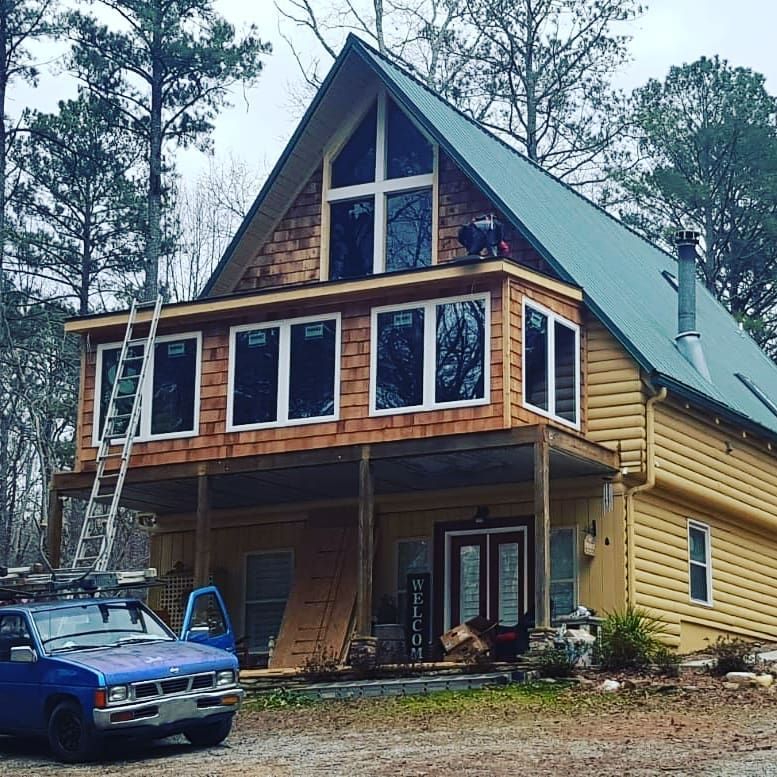 Wood-framed cabin under construction with blue truck and ladder in a wooded area