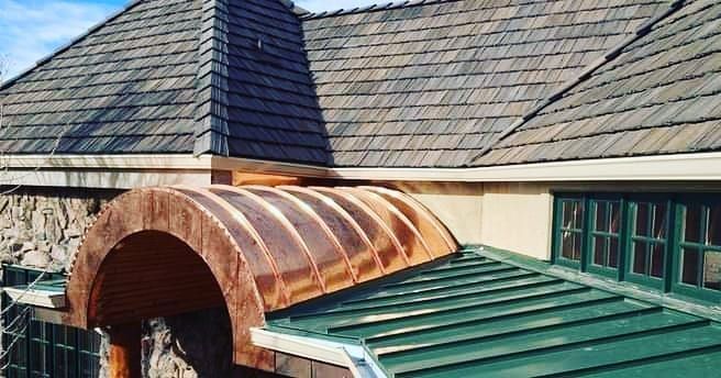 Rusty curved metal awning over green roof beside a shingled building with windows