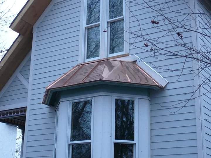 White house siding with a copper-roofed bay window and bare tree branches nearby