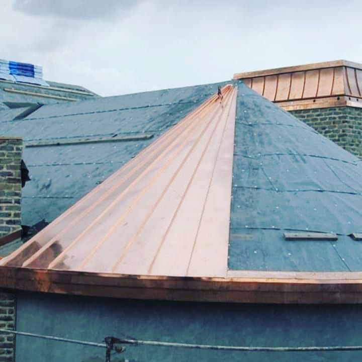 Copper-clad roof ridge and slate rooftop under overcast sky