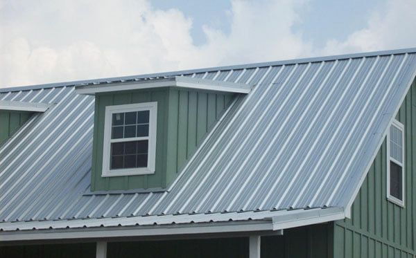 Green metal barn roof with a dormer window under a cloudy sky