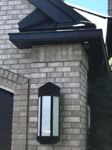 Black wall lantern on a gray brick house exterior under a dark roof overhang