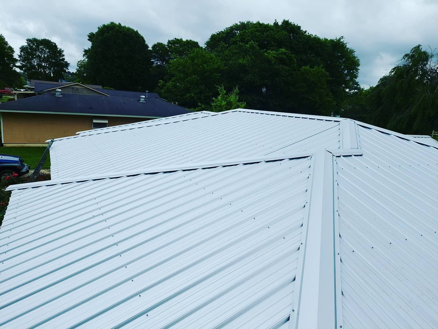 White metal roof with ridges viewed from above, with trees and houses in the background
