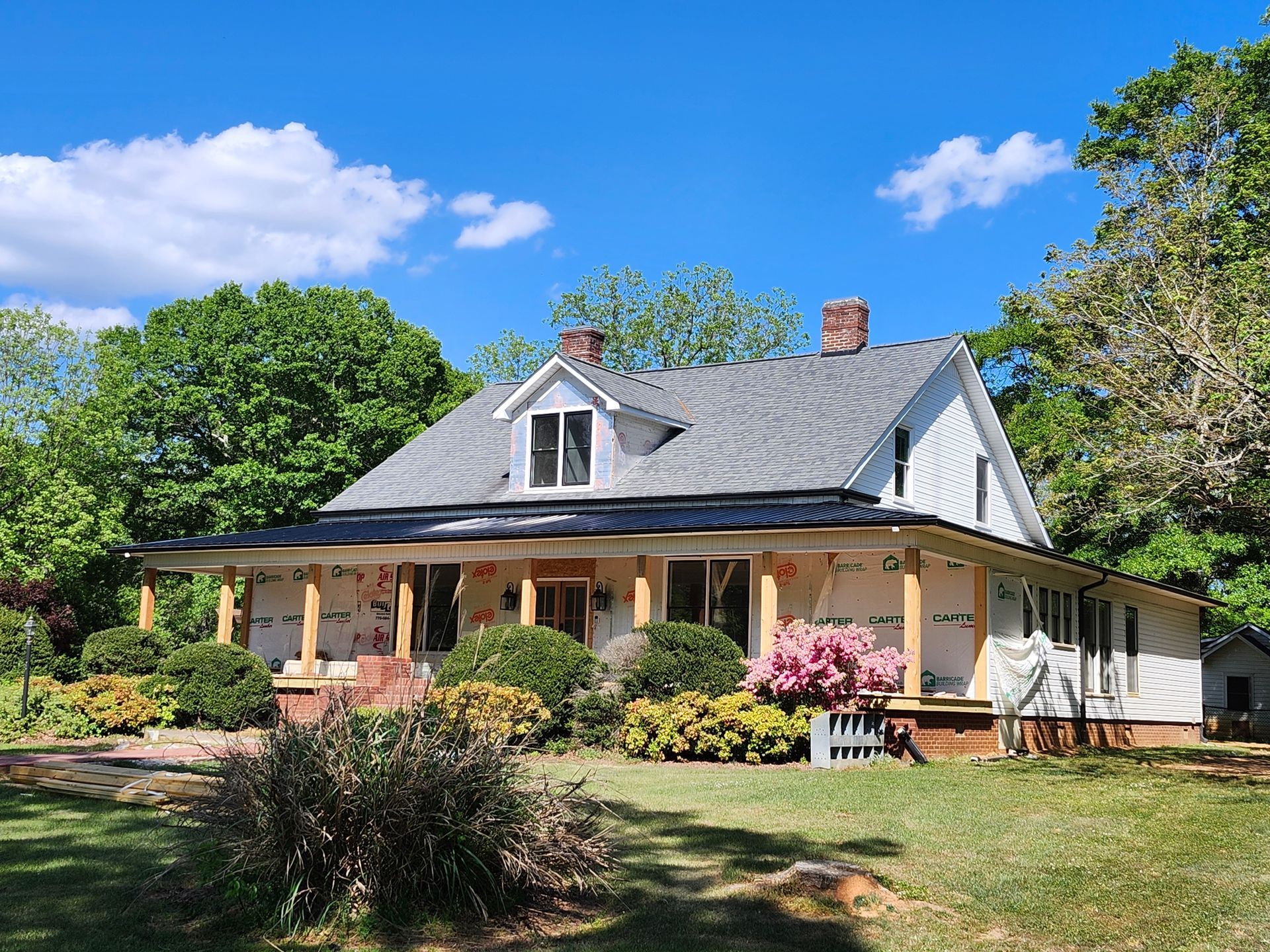 White cottage with a gray roof, brick porch, and colorful flowers in a sunny garden under a blue sky