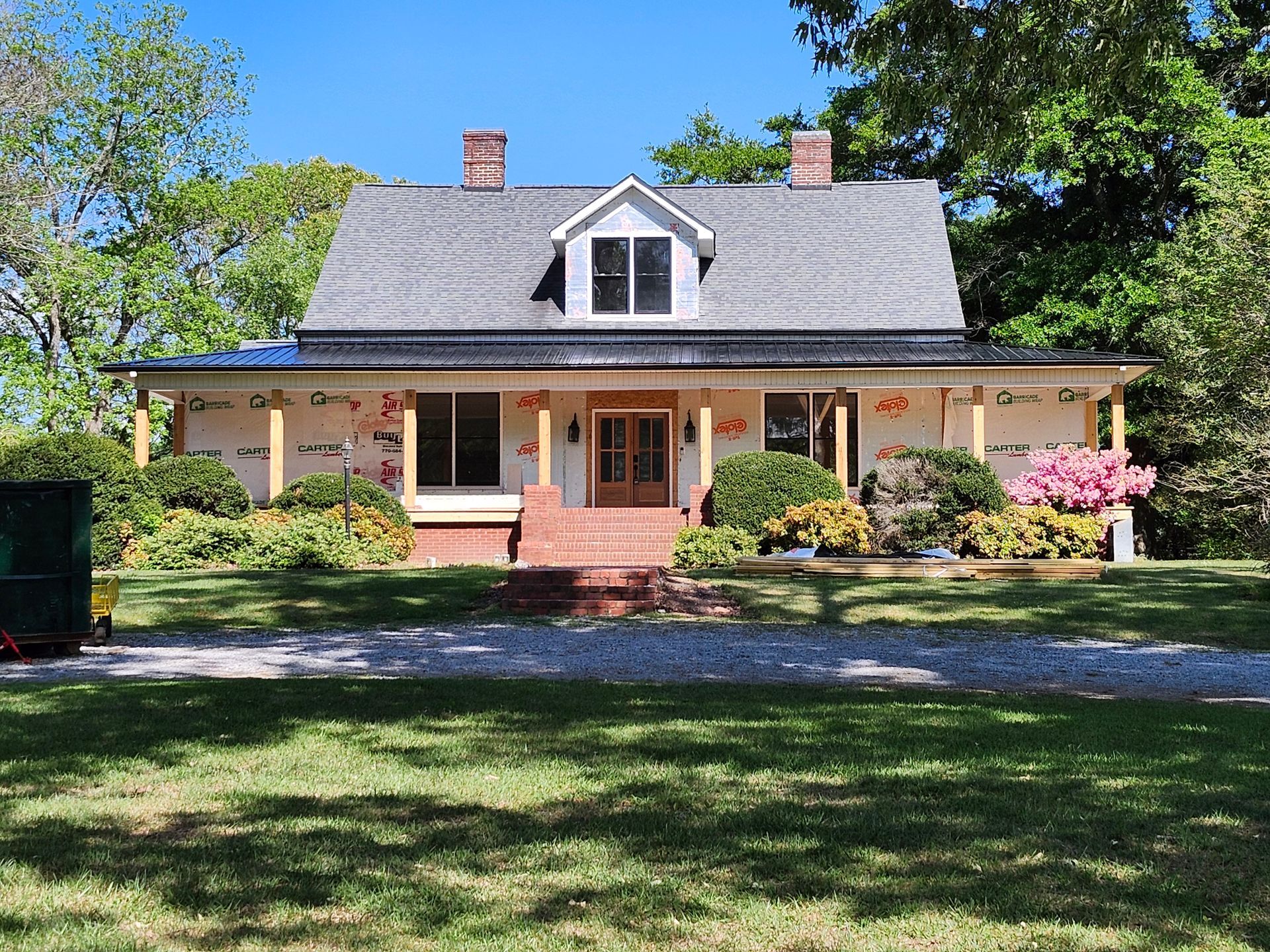 Large cream house with a gray roof, front porch, and brick steps, set behind a grassy yard and gravel drive.