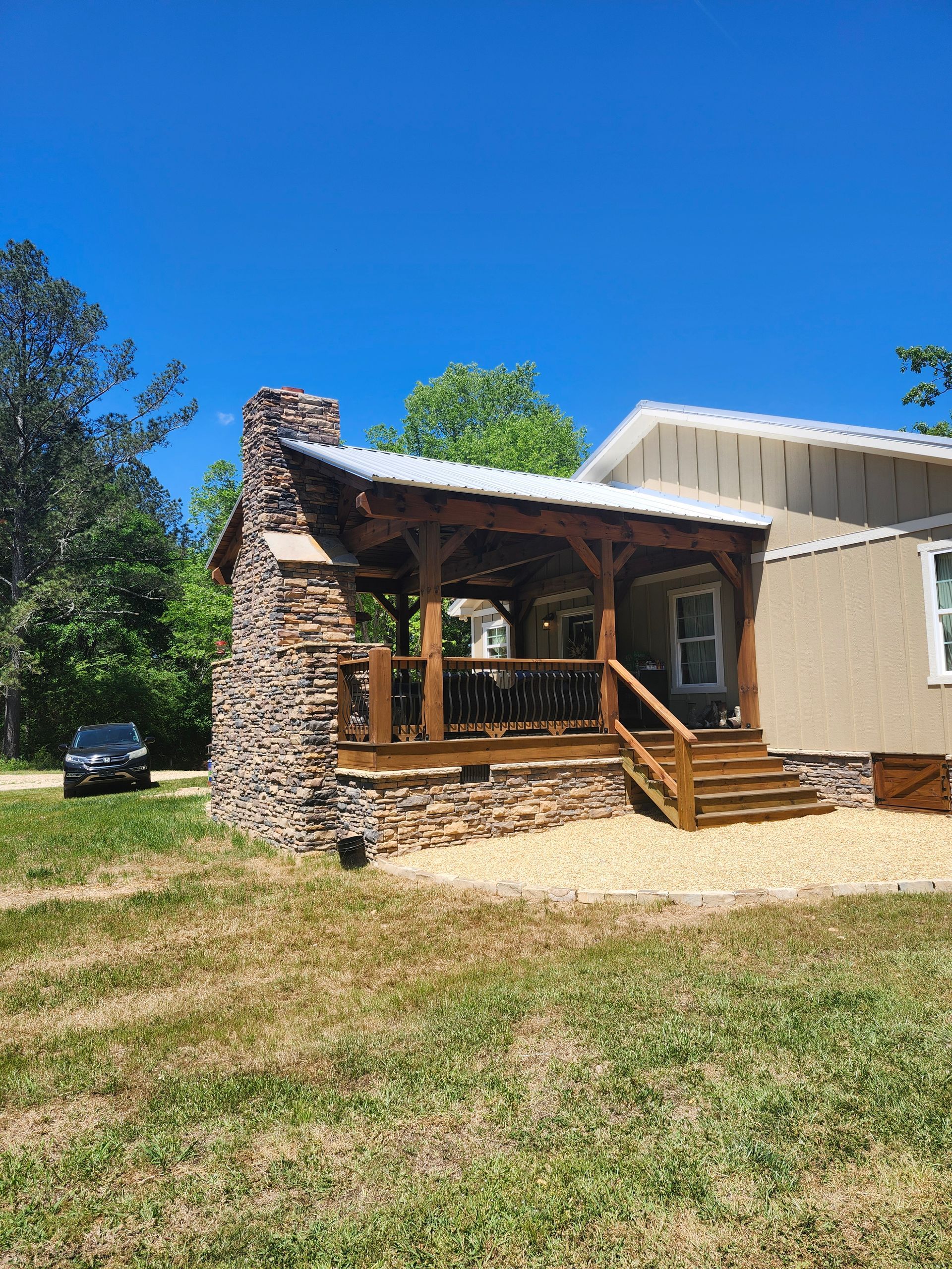 Small rustic cabin with stone chimney, wooden porch, and steps under a bright blue sky.