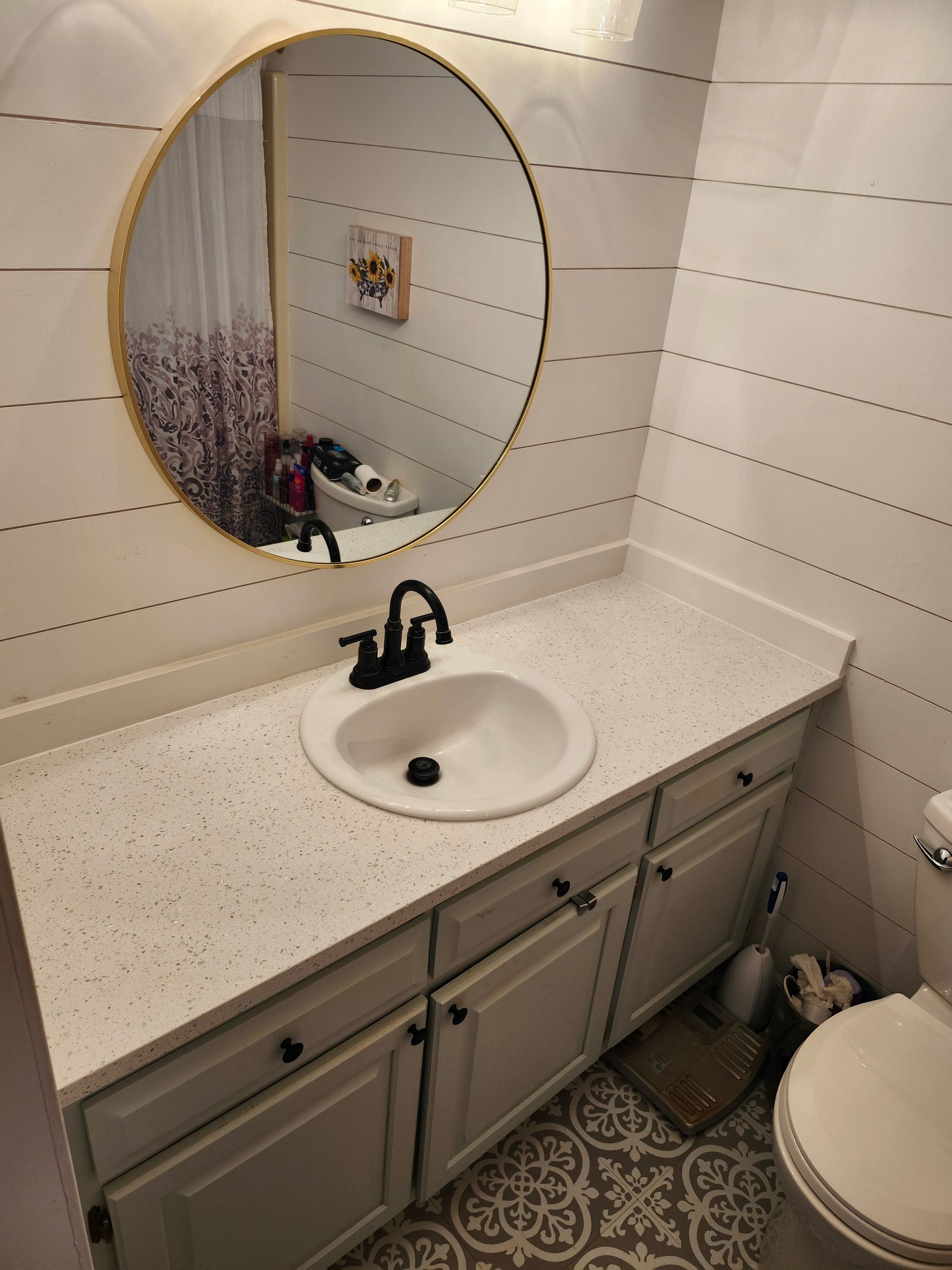 Small bathroom vanity with round mirror, white countertop, black faucet, and gray cabinets