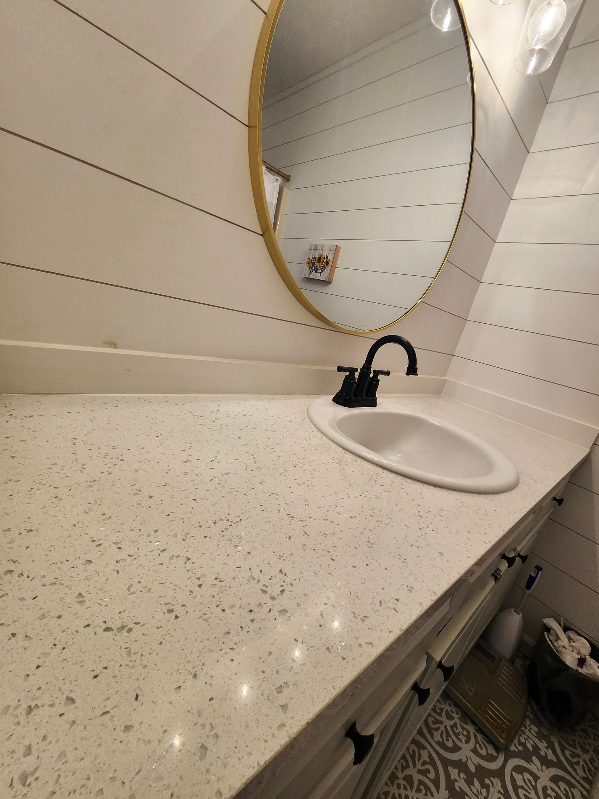 Small bathroom vanity with a white sink, black faucet, and speckled countertop beneath an oval mirror.