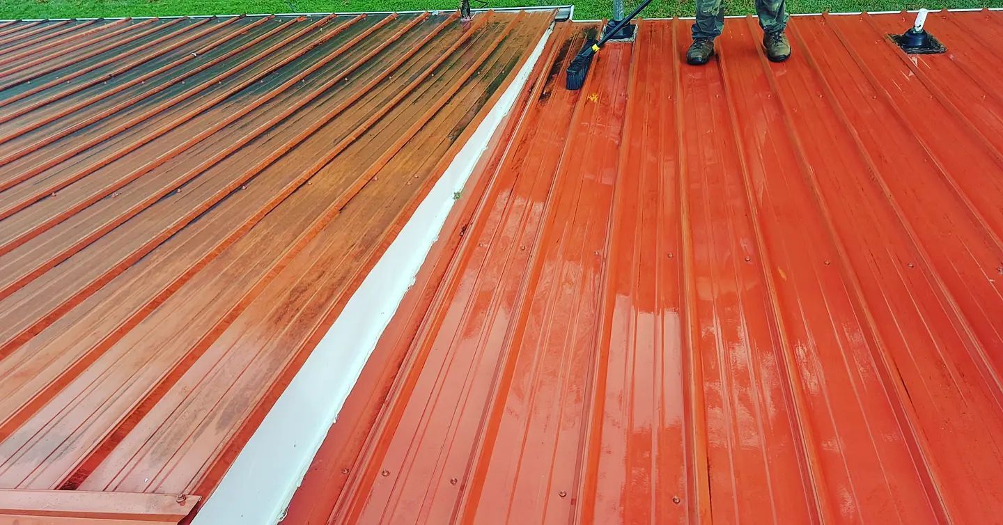 Workers applying red coating to a metal roof with rollers and a paint bucket