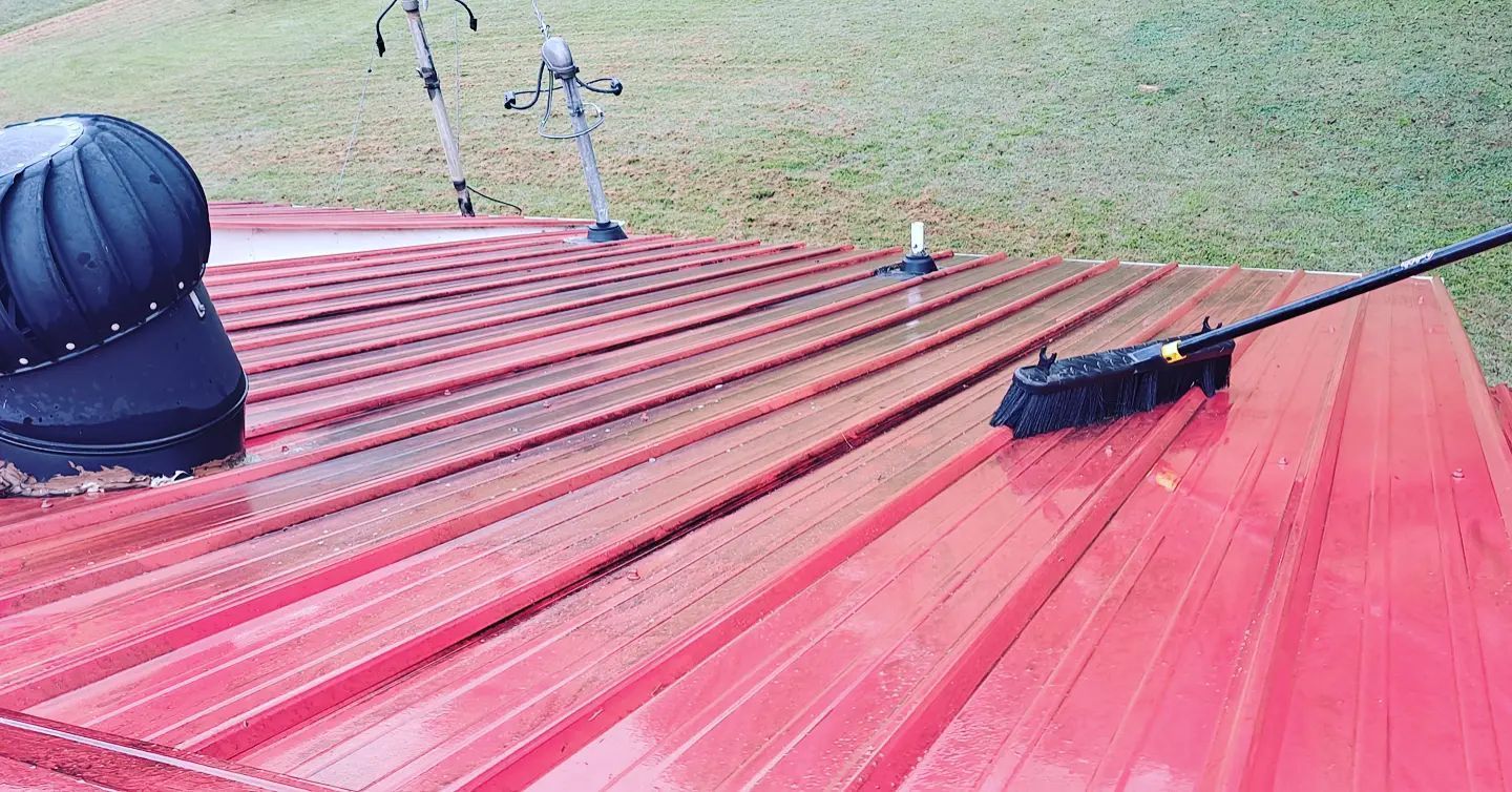 Red metal roof with vents and equipment under an open grassy hillside sky