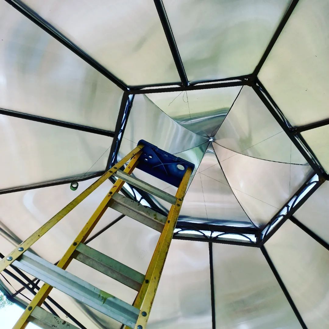 Looking up inside a metal tower with a yellow ladder leading to a white octagonal canopy.