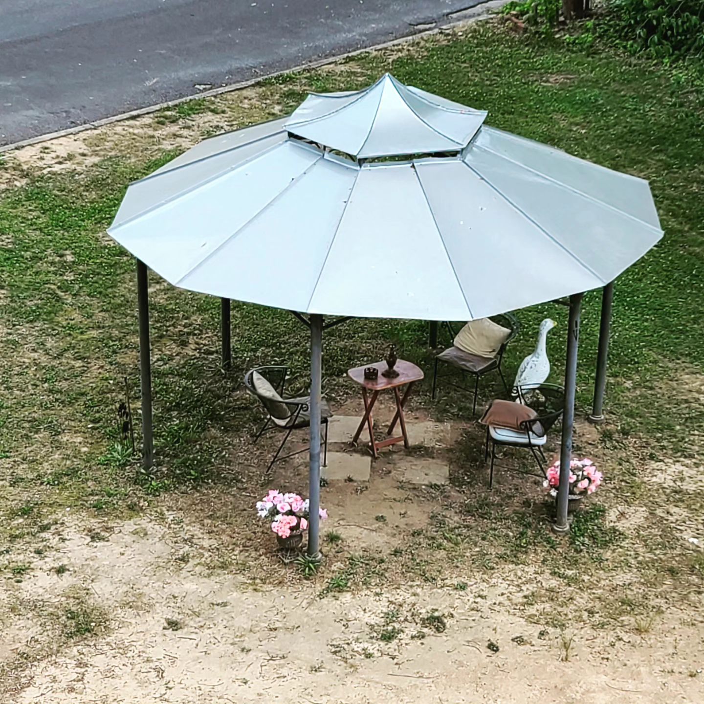 Small metal gazebo with a light gray roof and chairs in a grassy yard
