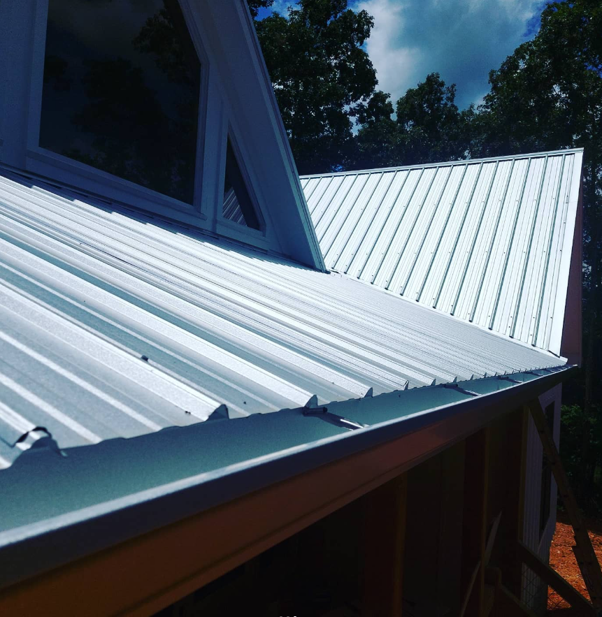 White metal roof on a house under a blue sky, with trees in the background