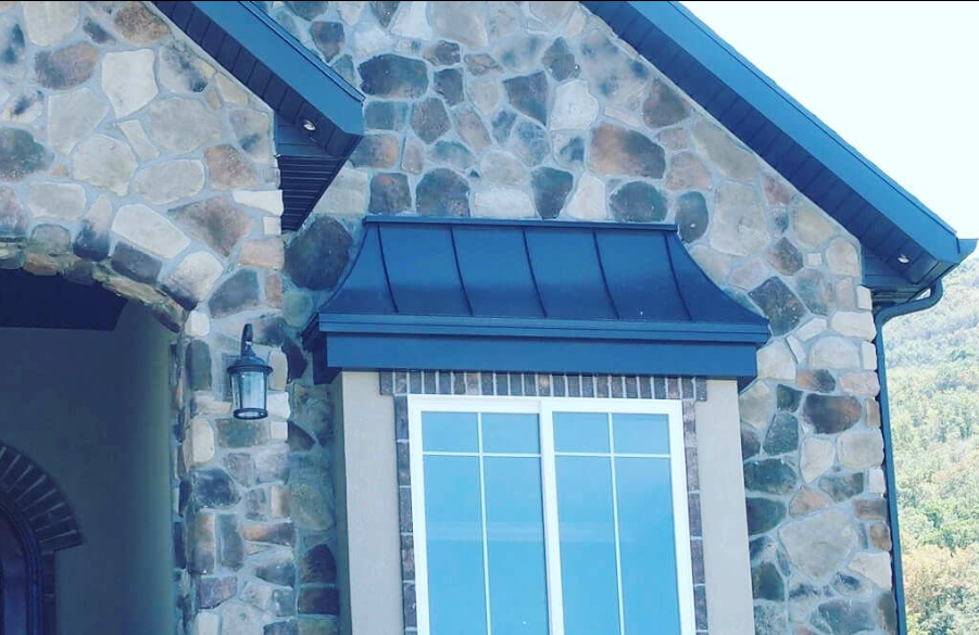 Stone house exterior with blue-trimmed window and dark metal awning under a gabled roof