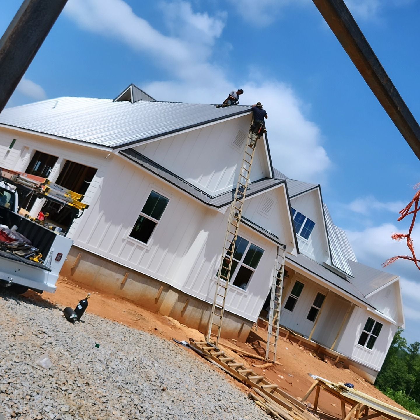 New white house under construction with a metal roof and ladder on a gravel lot under a blue sky