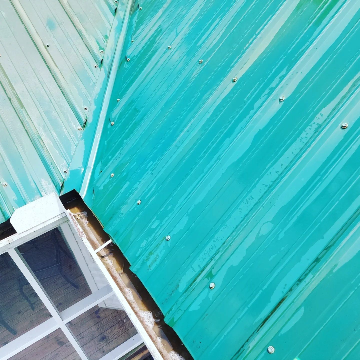 Turquoise metal roof beside a white-framed skylight window