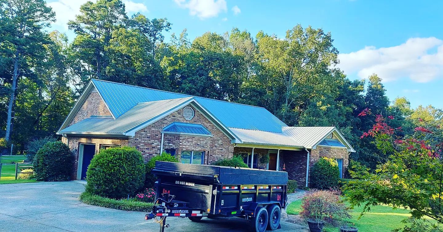 Stone house with a blue metal roof and black truck parked in front, surrounded by trees and shrubs