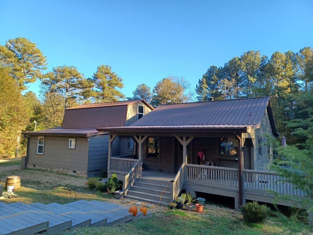 Small cabin with porch and steps in a wooded yard, under a blue sky