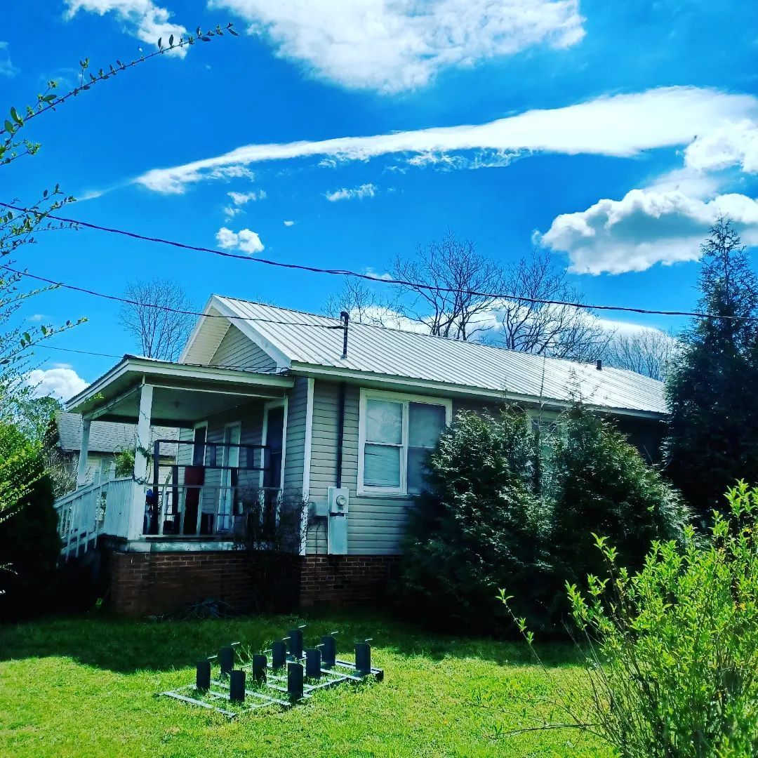 Small white house with a porch, green lawn, and bright blue sky with clouds