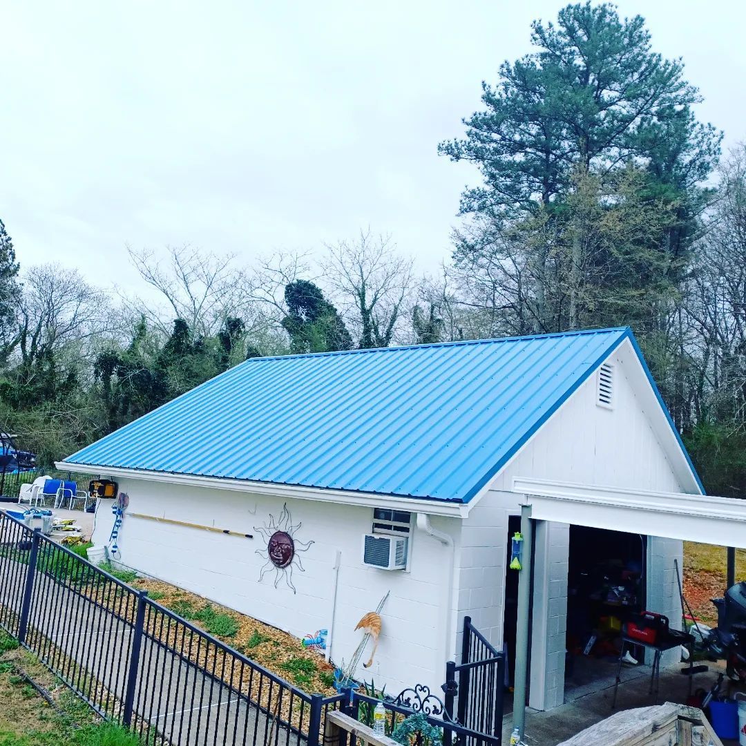 White house with a bright blue metal roof beside a fenced yard and trees