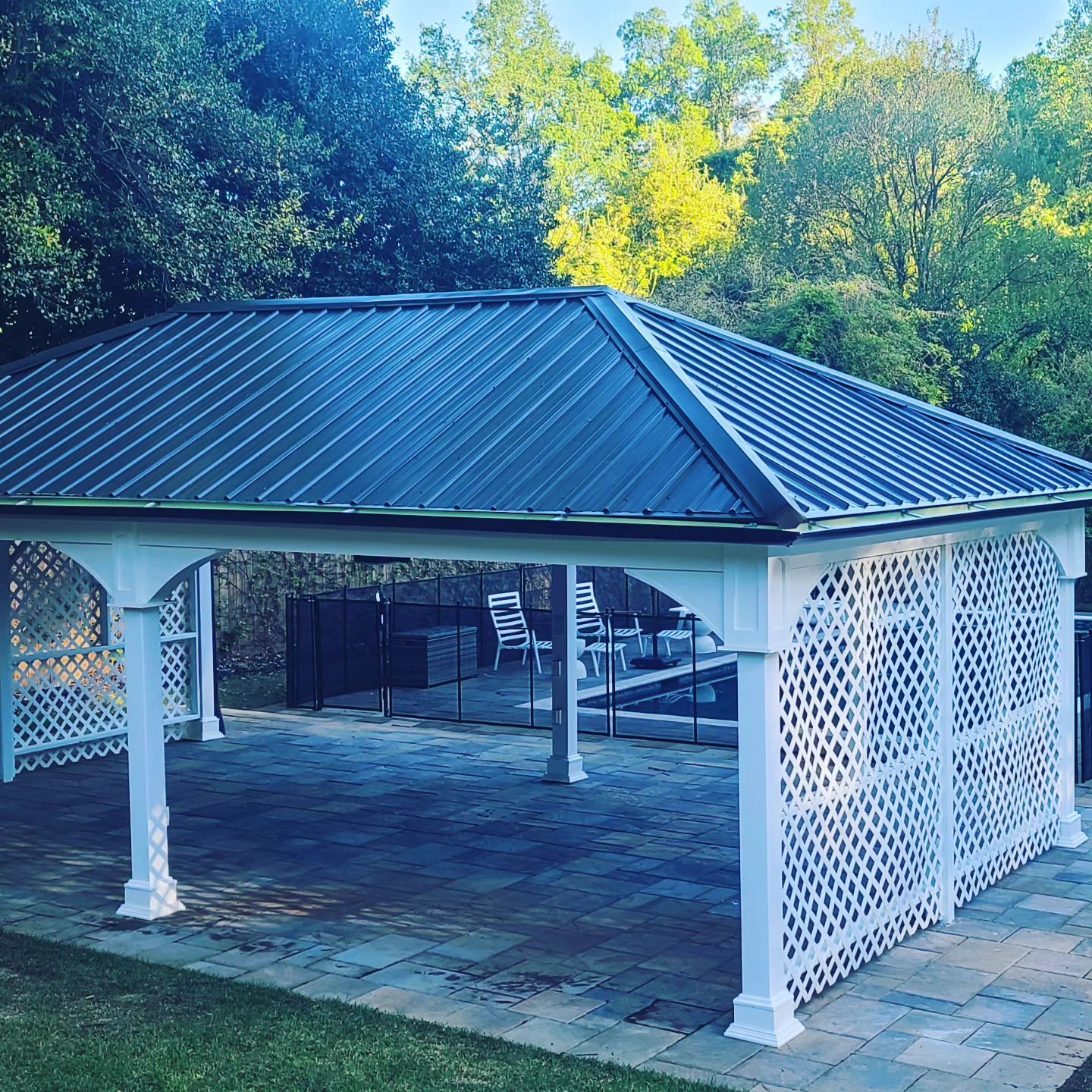 White gazebo with blue metal roof and lattice sides in a wooded park setting