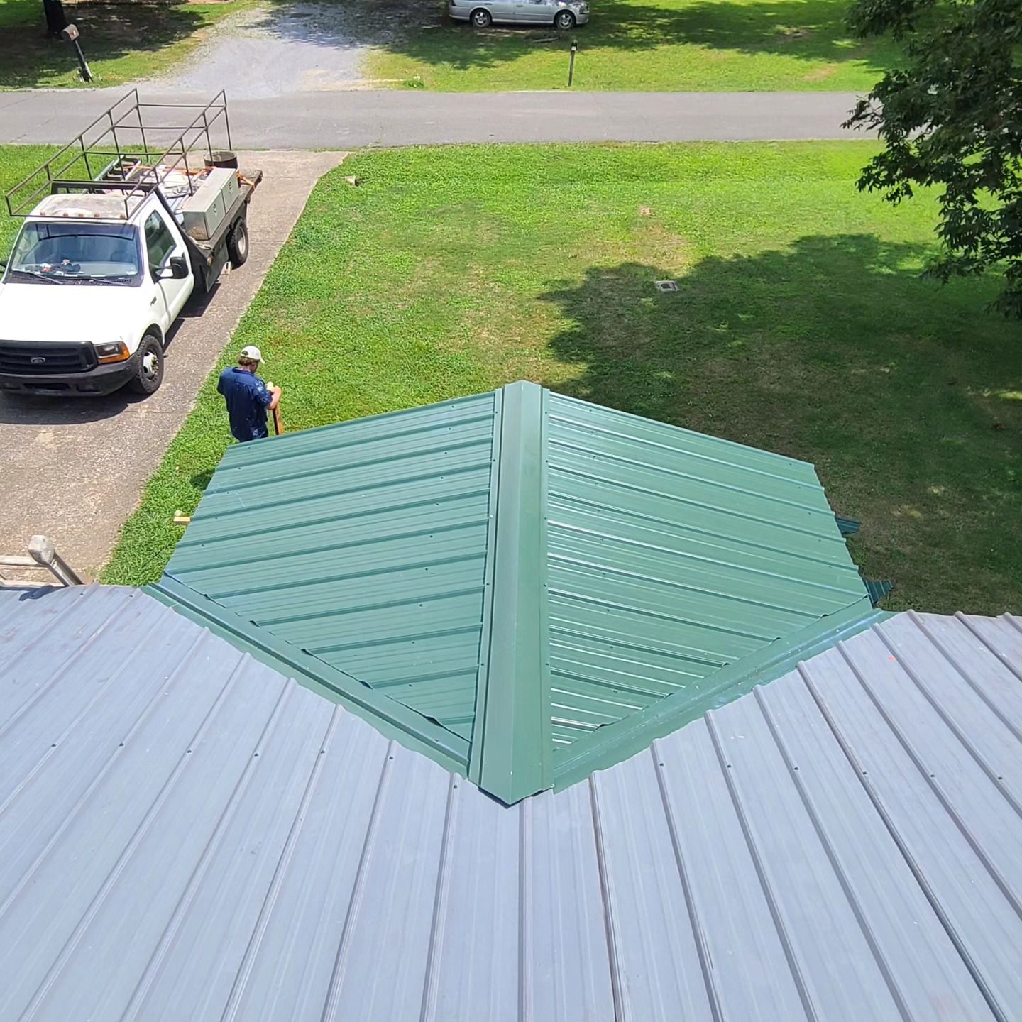 Roof with green metal peak, light gray panels, and a person standing on the lawn near a driveway.