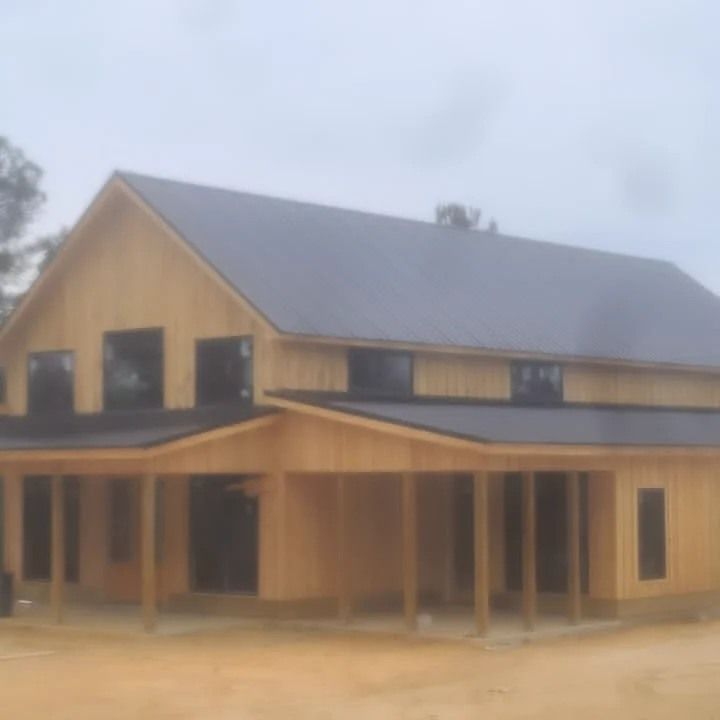 Wooden house with a dark gray roof and covered porch on a dirt lot