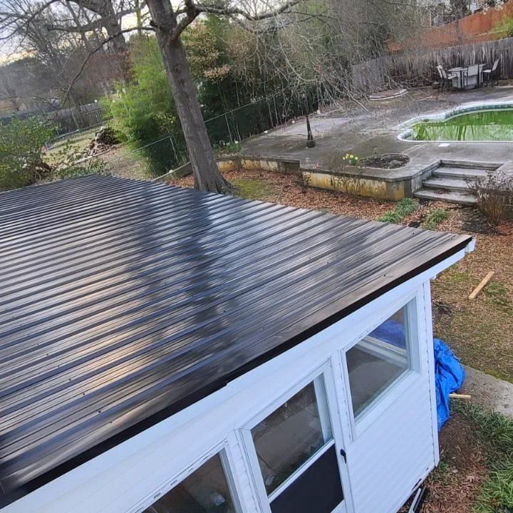 Backyard shed with a black metal roof, white walls, and a pool in the background