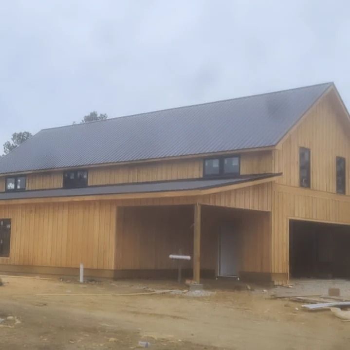 Wooden barn-style house with a dark roof and covered porch on a muddy construction site