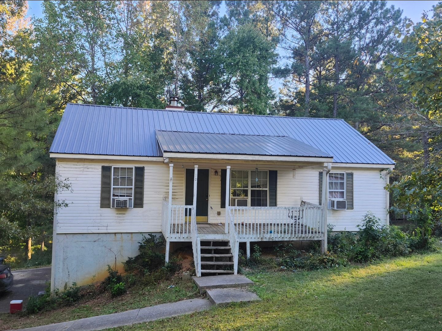 White house with blue metal roof and small porch in a wooded yard