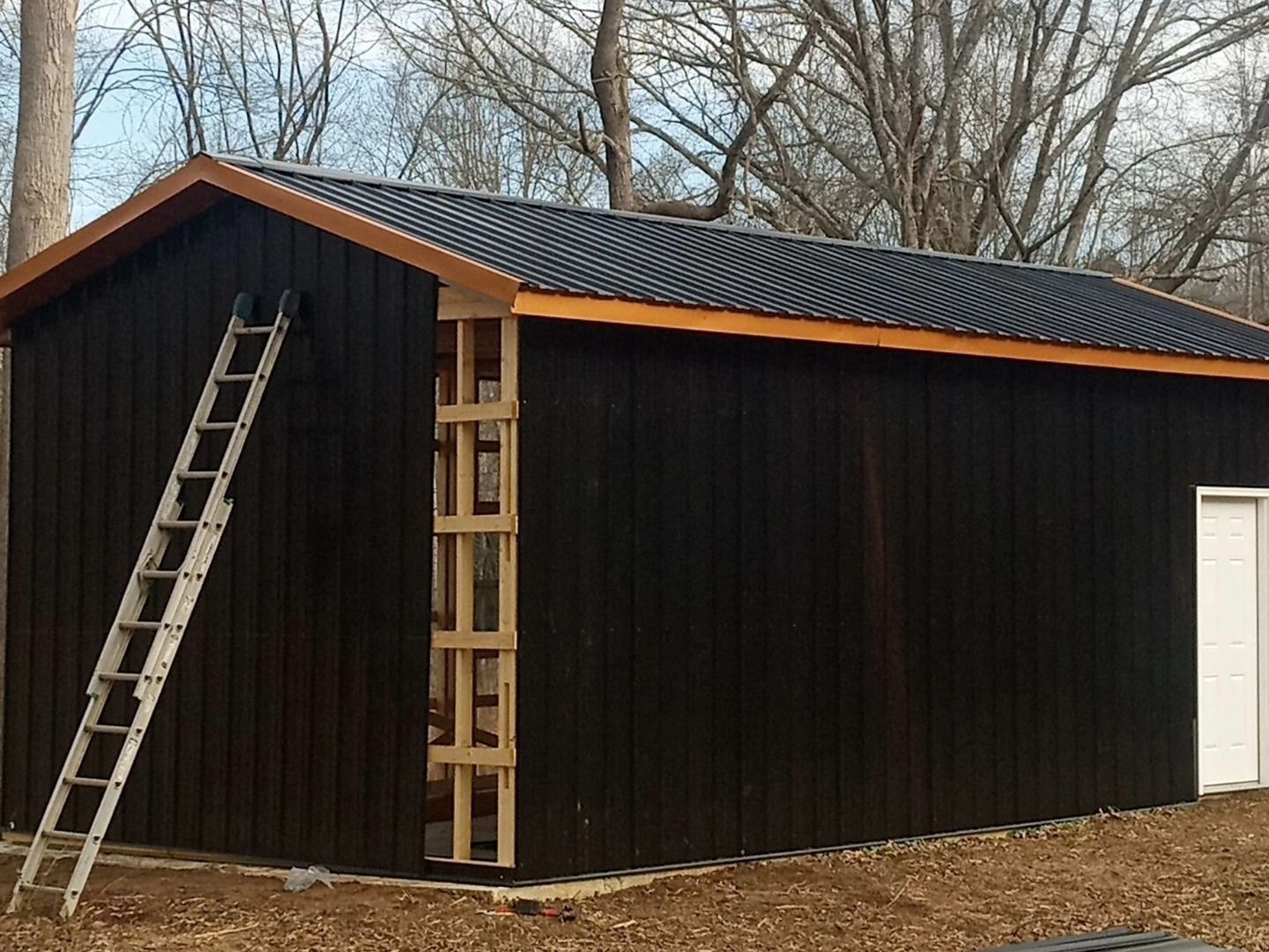 Black shed under construction with ladders leaning against the side and back.