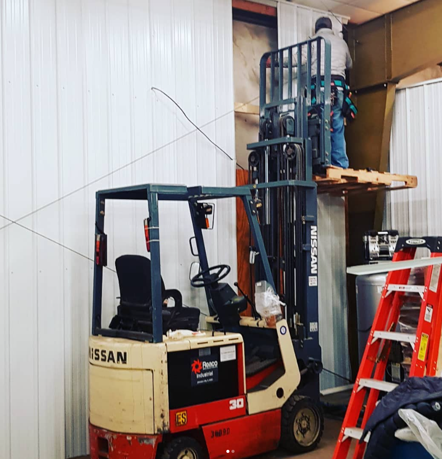 Red Nissan forklift in a warehouse beside a red ladder and shelving.