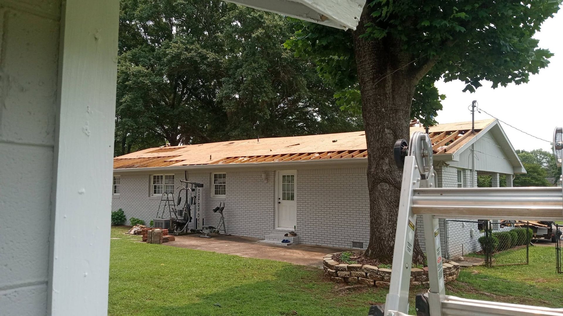Small gray house with an orange roof, viewed from a porch with a large tree and green lawn in front.