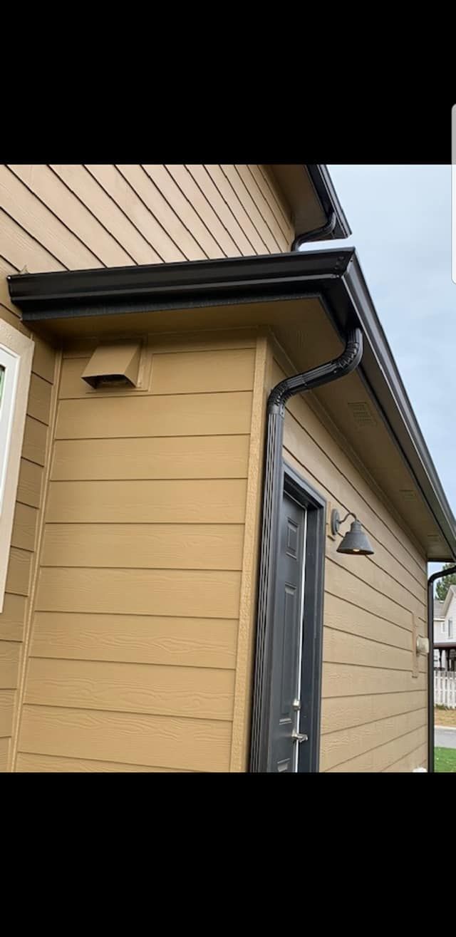 Yellow house exterior with dark trim, gutter, and side door under an overhang