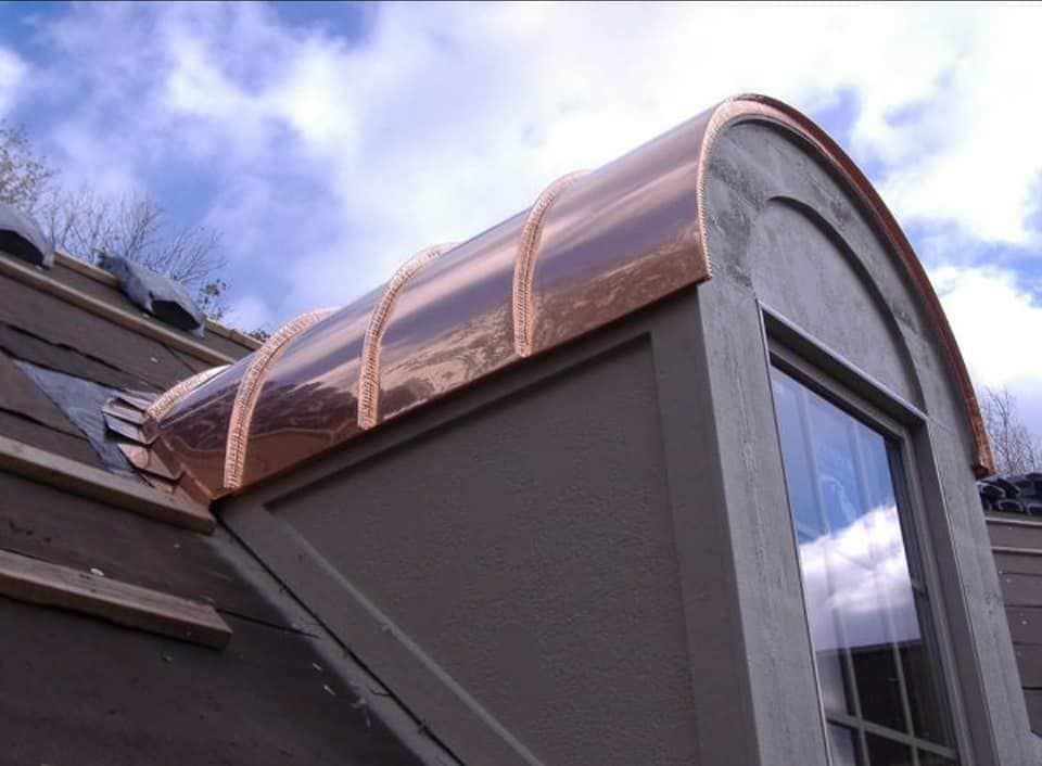 Dormer window with a curved copper roof on a gray house under a cloudy sky