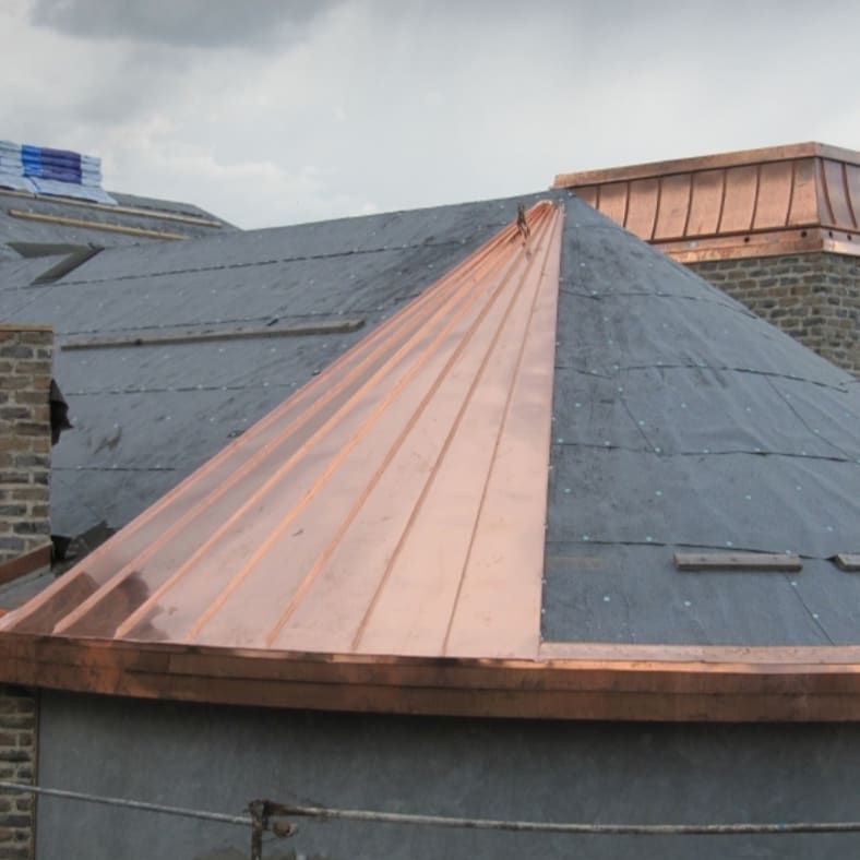 Copper-colored standing seam roof section on a dark gray rooftop under an overcast sky
