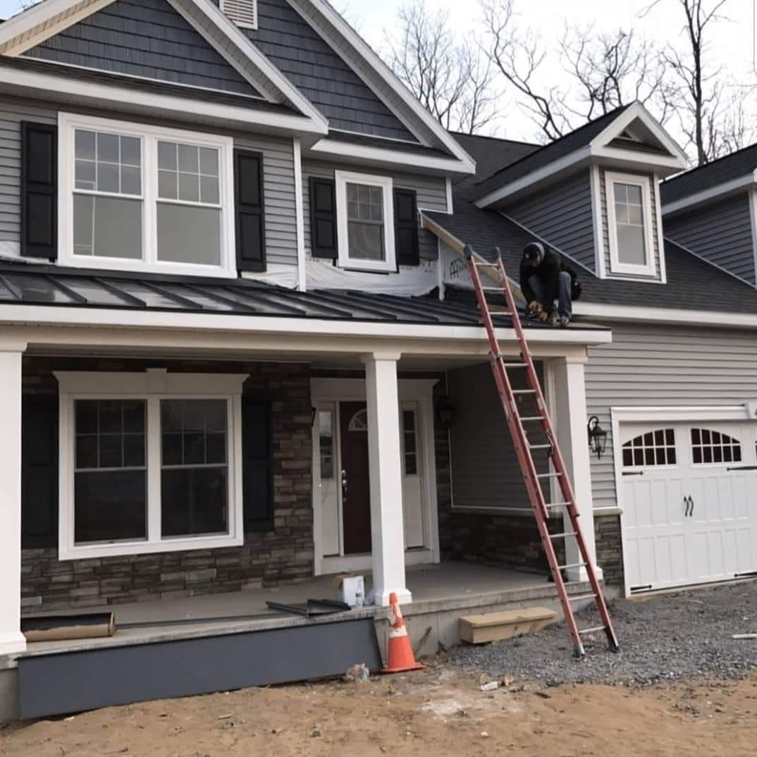 Two-story house exterior with a worker on a ladder repairing the roof over the garage